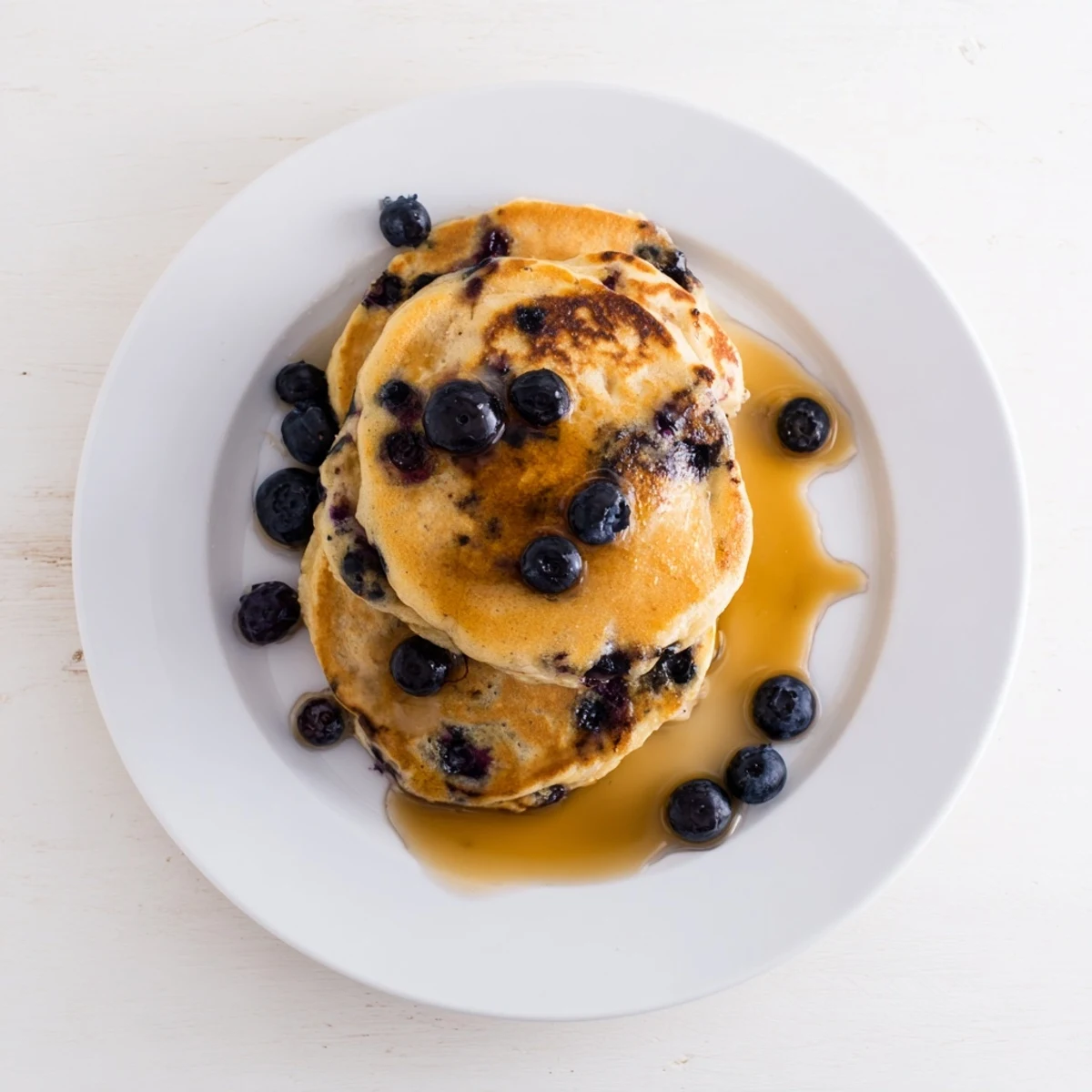 Fluffy breakfast pancakes made with Greek yogurt and juicy blueberries served with syrup on a rustic wooden table