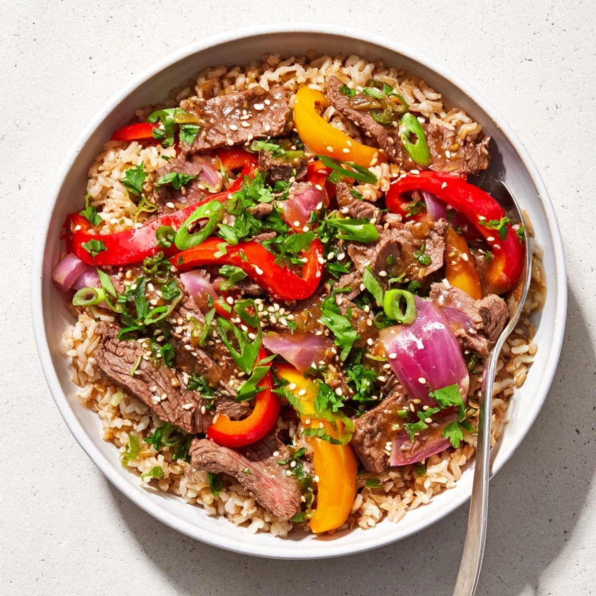 Protein-packed healthy beef and pepper rice bowl garnished with fresh cilantro, sesame seeds, and savory garlic-ginger glaze