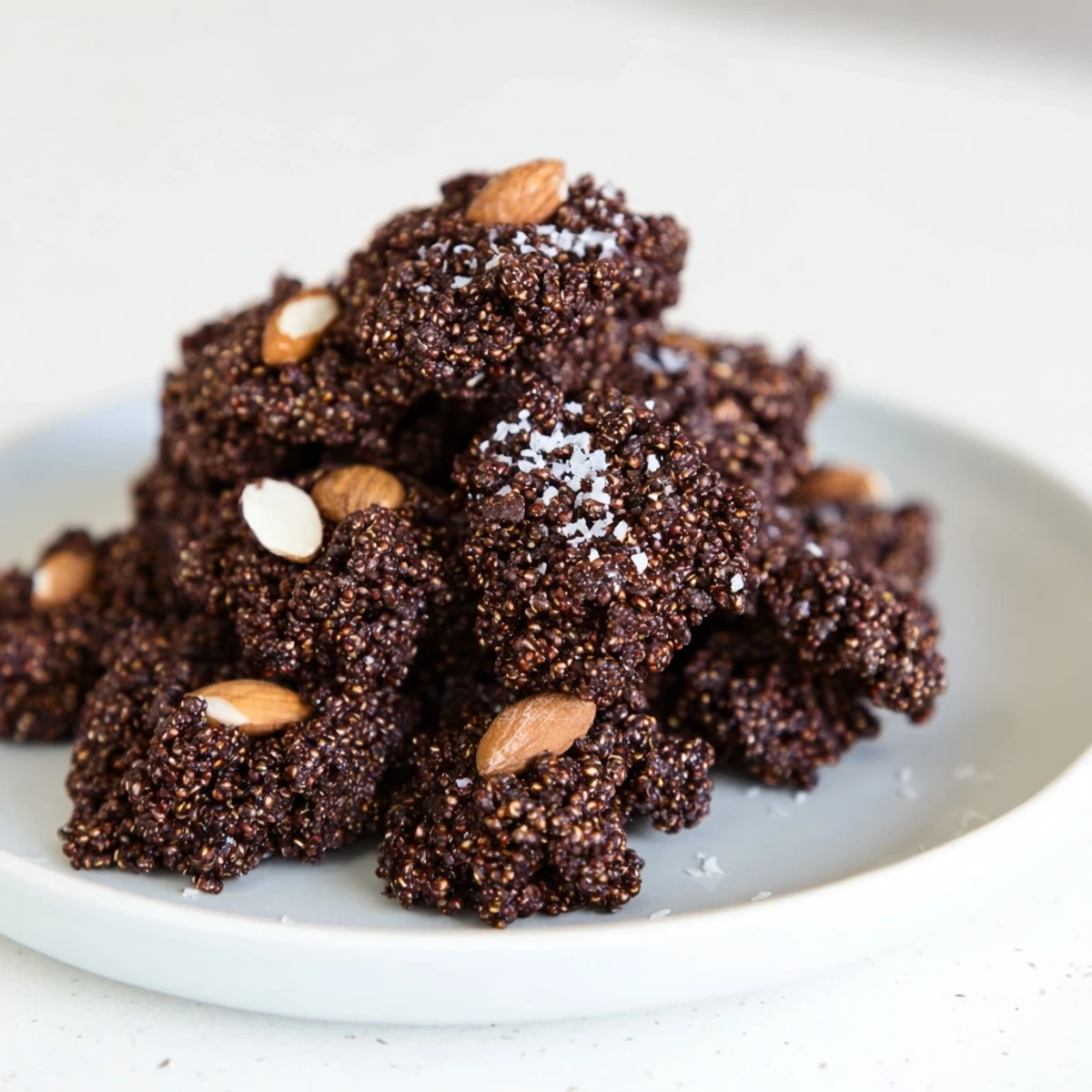 Dark chocolate quinoa crisps arranged on a white plate with glossy chocolate coating and toasted golden quinoa bits visible