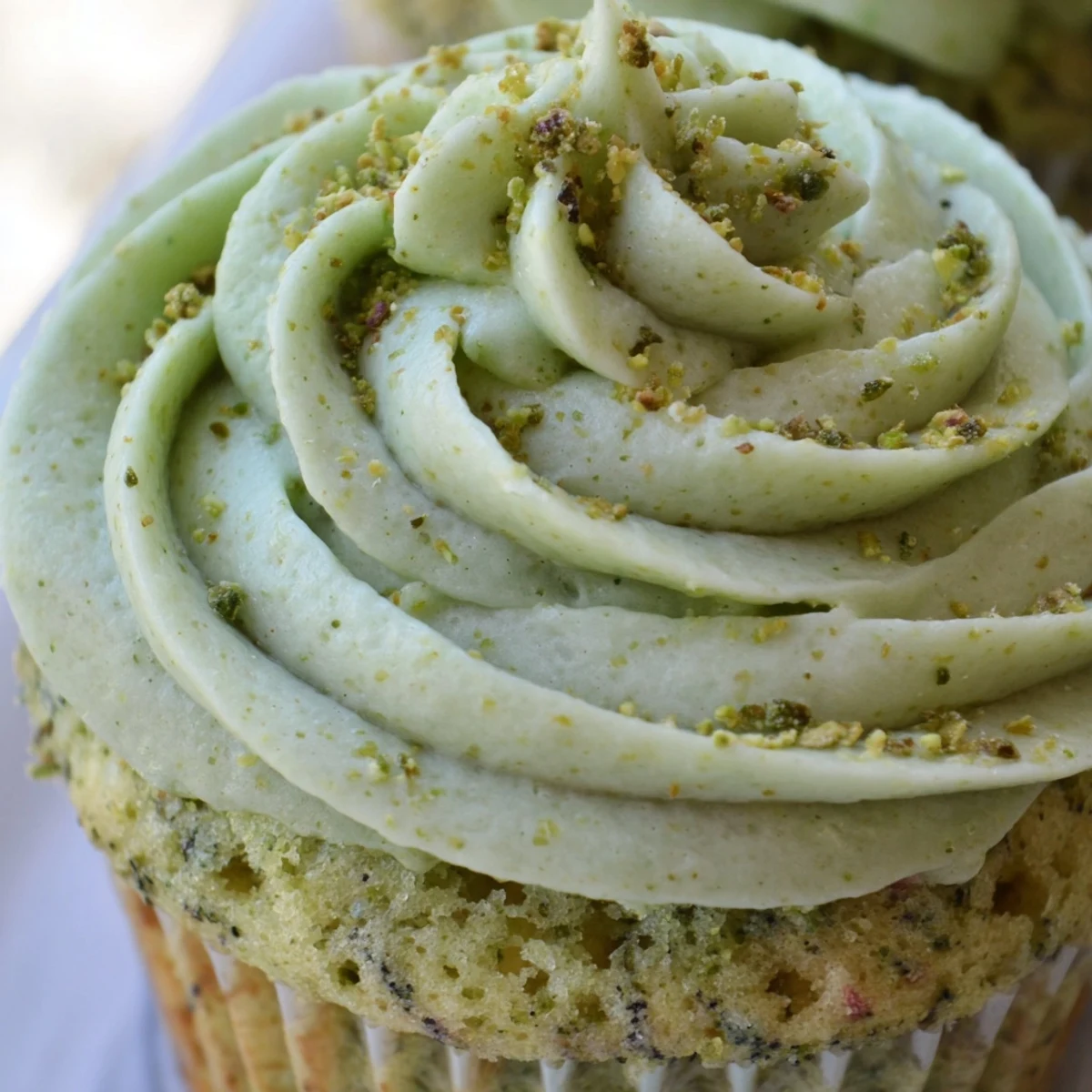 Soft pistachio cupcakes topped with creamy green buttercream frosting and chopped nut garnish