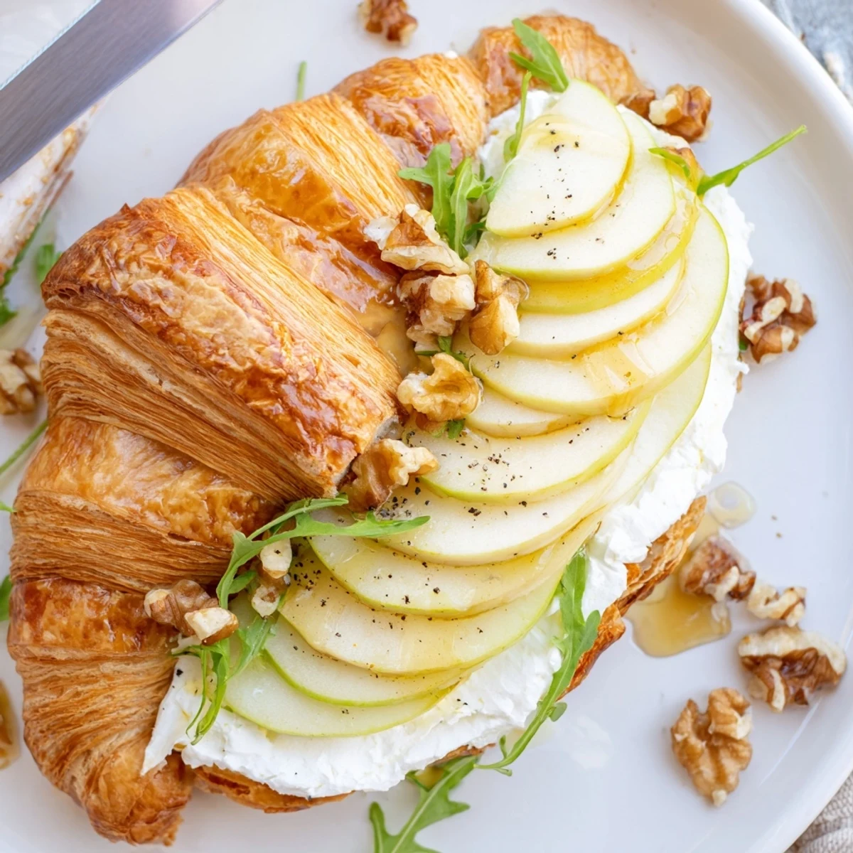 Toasted Apple Goat Cheese Croissant Sandwich sliced in half, revealing creamy, crunchy layers.