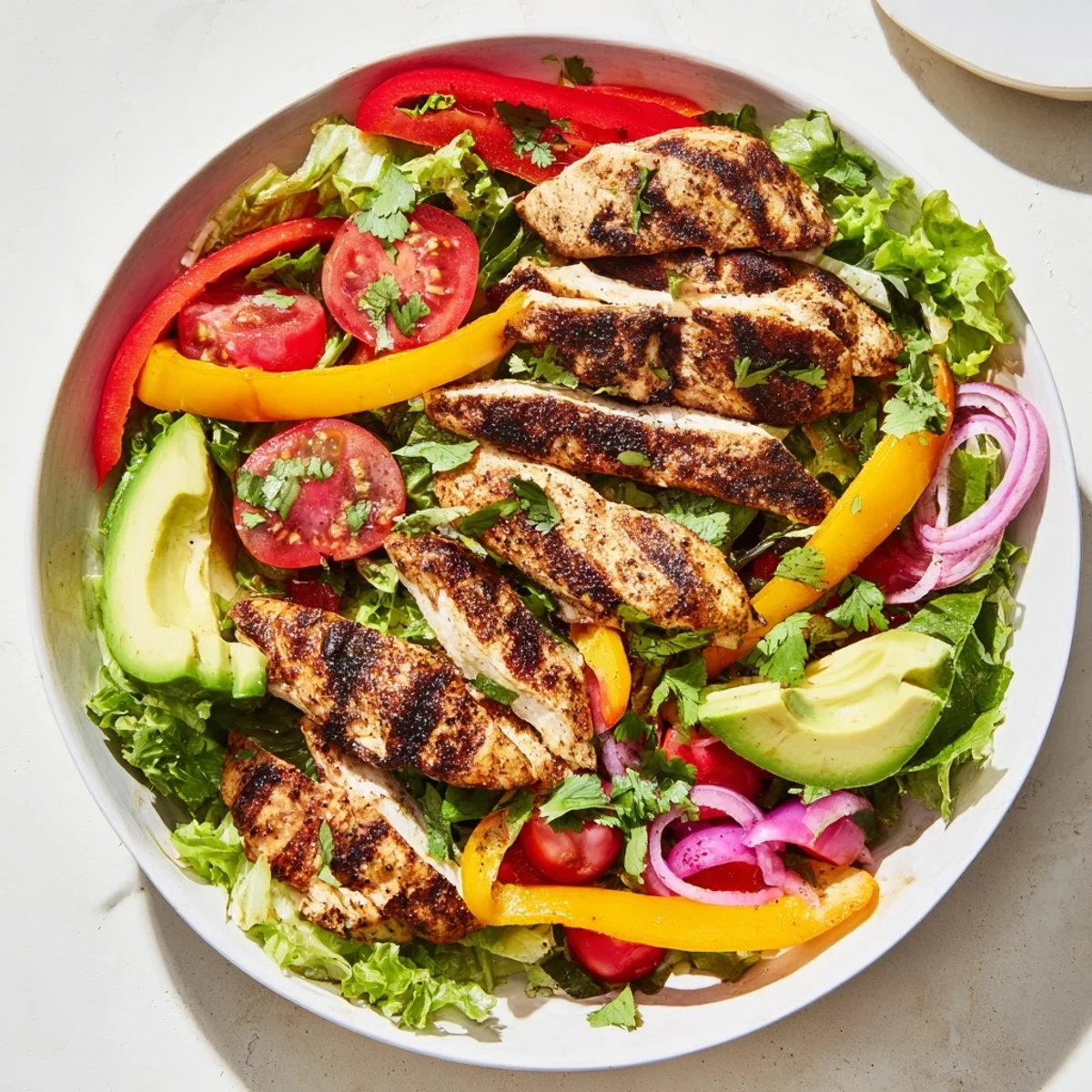 Sliced grilled fajita chicken atop vibrant Tex-Mex salad with red peppers, onions, cherry tomatoes, and creamy avocado