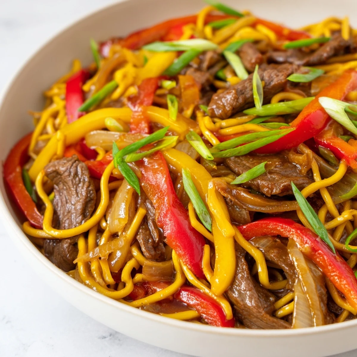Plated beef chow mein featuring tender meat strips, crisp vegetables, and glossy egg noodles