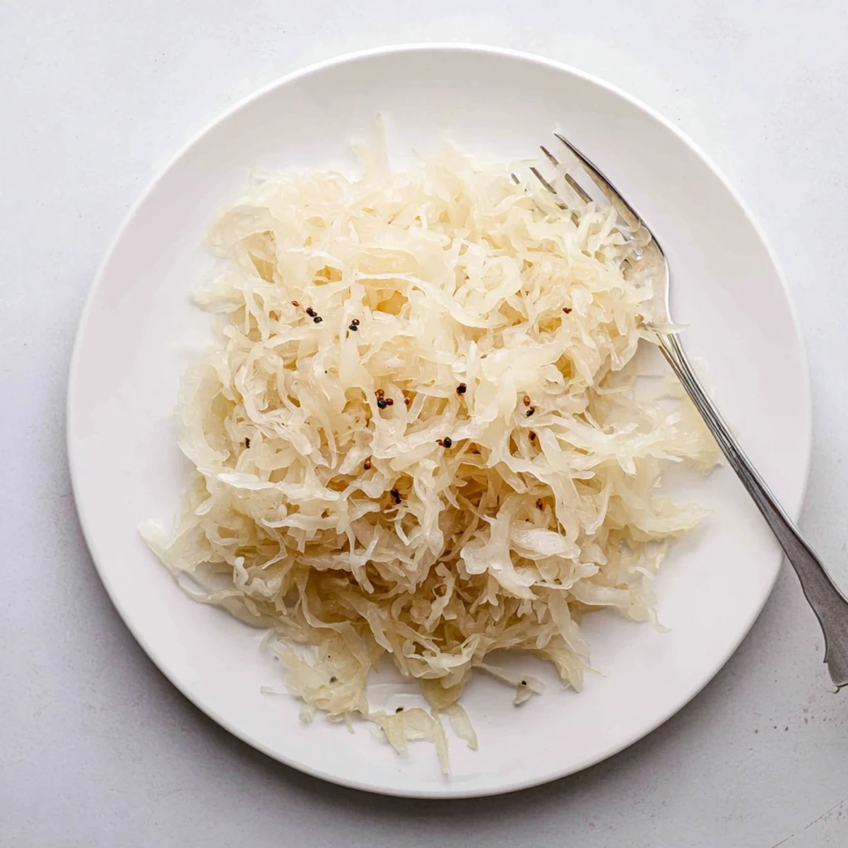 Tangy German sauerkraut mounded in a white bowl alongside bratwurst and mustard