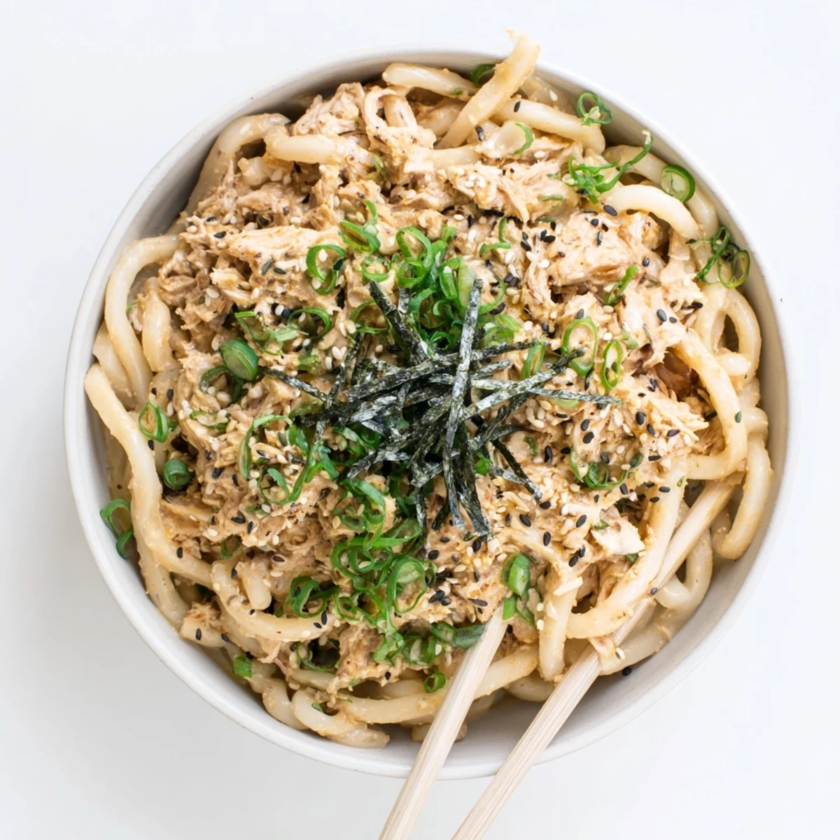 Steaming bowl of spicy tuna udon noodles garnished with fresh scallions and sesame seeds
