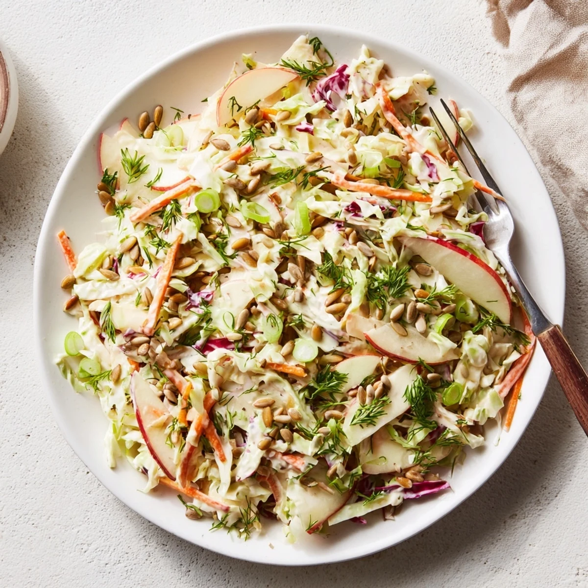 Fresh apple coleslaw served in a white bowl with vibrant green and red cabbage shreds