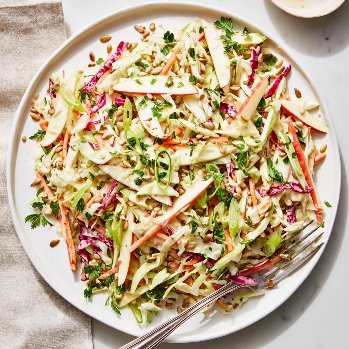 Creamy apple coleslaw topped with toasted sunflower seeds featuring crisp julienned apples and shredded carrots