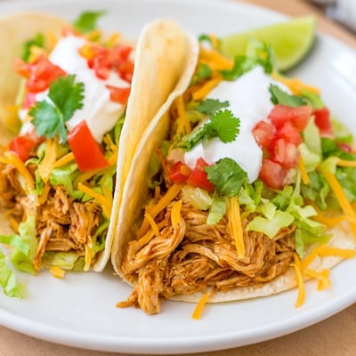 Slow cooker ranch chicken tacos loaded with sour cream lettuce and diced tomatoes